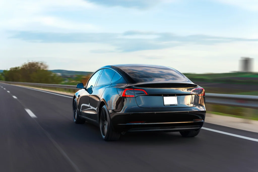 Rear view of a black Tesla Model 3 driving on a highway, representing fuel-efficient electric vehicles.