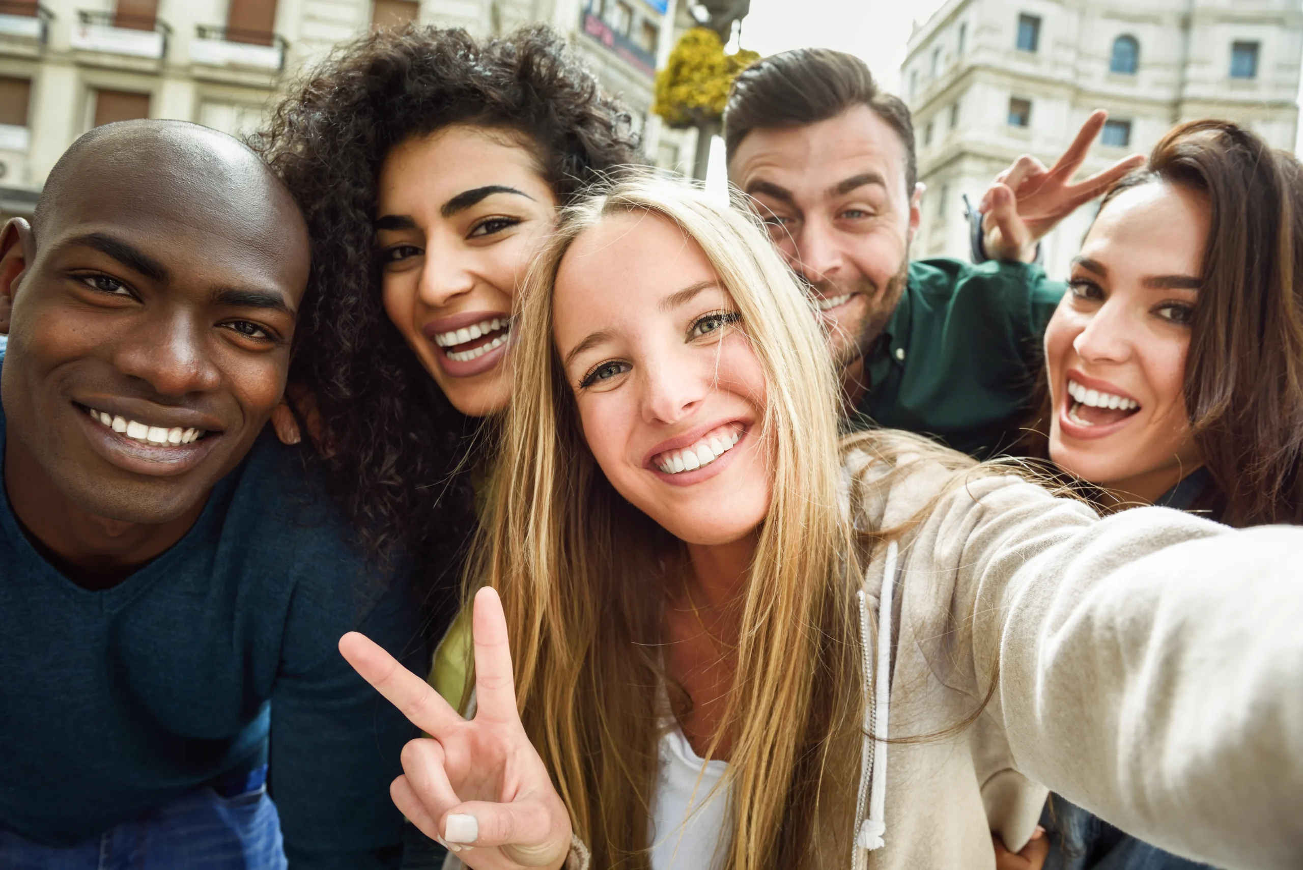 A diverse group of five young women smiling and taking a selfie in an urban setting, showing off their healthy white teeth. One of the women makes a "peace and love" sign with her fingers.
Title: Confident Smiles with ProvaDent.