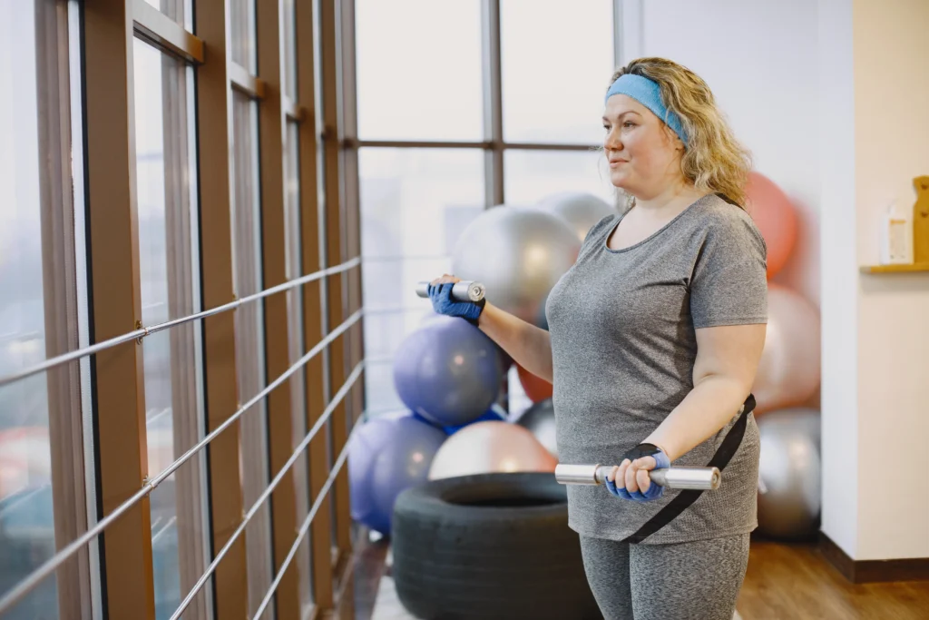 Older woman with a headband exercising with light dumbbells in a gym setting.