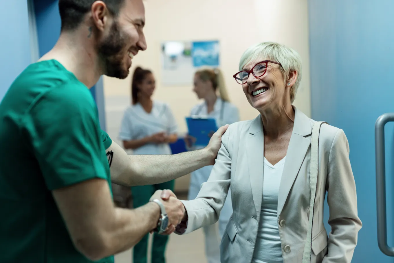 A smiling senior woman shaking hands with a healthcare professional, with other medical staff blurred in the background. The text overlay reads: "Telehealth: Bridging Gaps in Healthcare Access. Emerging telehealth and remote patient monitoring technologies also hold promise for enhancing healthcare access for older adults, especially those in rural or underserved areas. Wearable devices and home-based sensors can track vital signs, physical activity, and other health indicators, allowing healthcare providers to monitor patients remotely and intervene proactively. This not only leads to better health outcomes but also helps reduce healthcare costs while improving the overall quality of life for seniors."